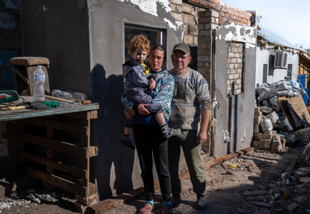 Mother holds her son & stands with her husband.