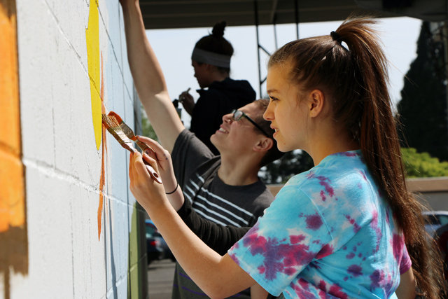Youth take turns painting portions of a mural