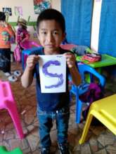 Student holding up salt painting for letter "S"