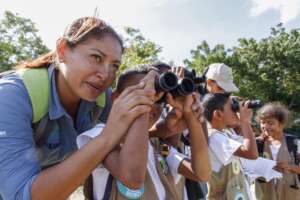 A ranger helps a child spot a bird with binoculars