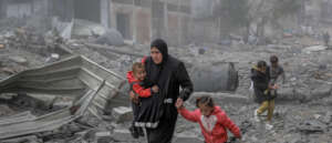 Mother walking through rubble with her children.