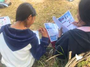 Lao girls read educational booklets given by AAT