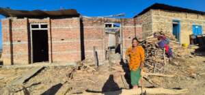 A woman cuts wood in front of her unfinished house