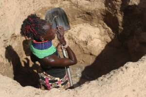 A woman scoping the sand from a shallow well