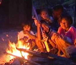 Children sit around litted flame to keep warm