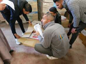Four men are looking through a box in a warehouse.
