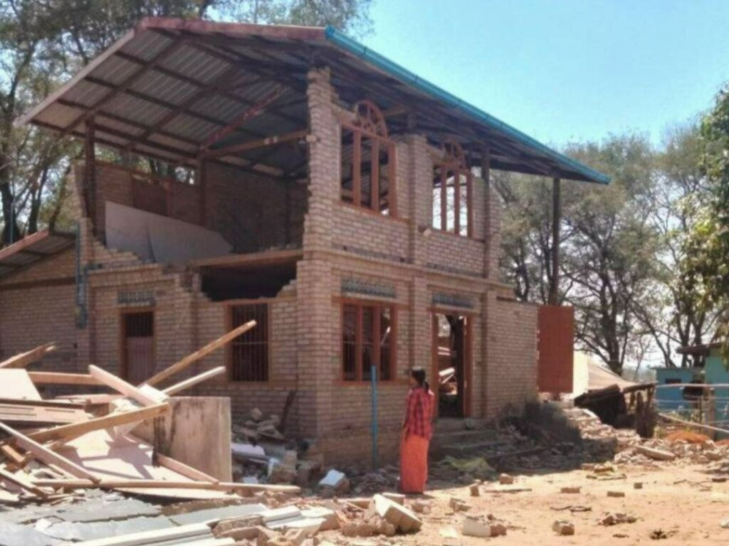 A woman standing in front of a collapsed house