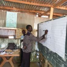 A teacher practices handwriting pattern on a board
