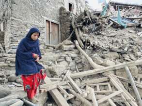 A girl stands beside a damaged house