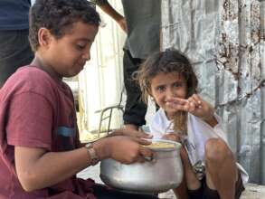Two children share a pot of food as the girl smile