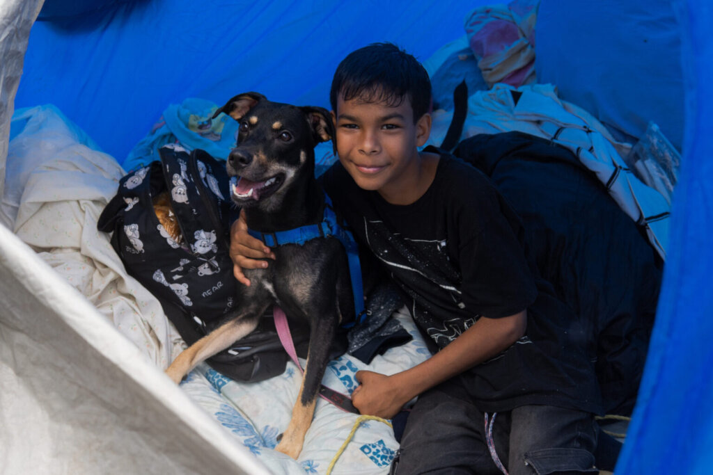 A boy shelters in a tent with his dog
