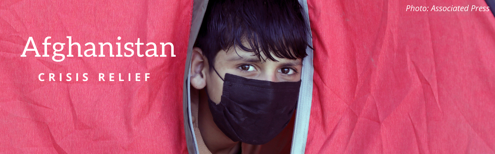 A boy wearing a face covering looks out of a tent.